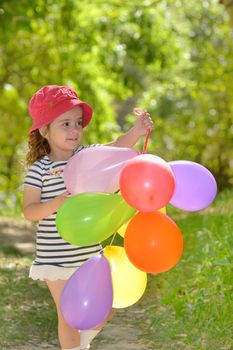 girl plays in summer park with colorful balloons