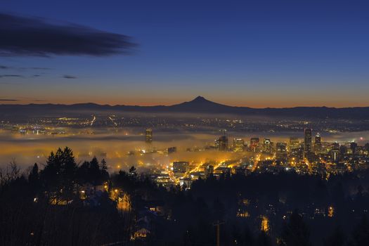 Thick Fog Rolling at Dawn over cityscape of downtown Portland Oregon with city lights and silhouette of Mt Hood