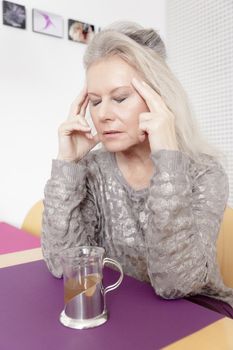 An image of a best age woman with headache and a cup of tea