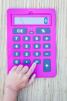 pink calculator on traditional mat with white space on the screen, hand pushing equal button