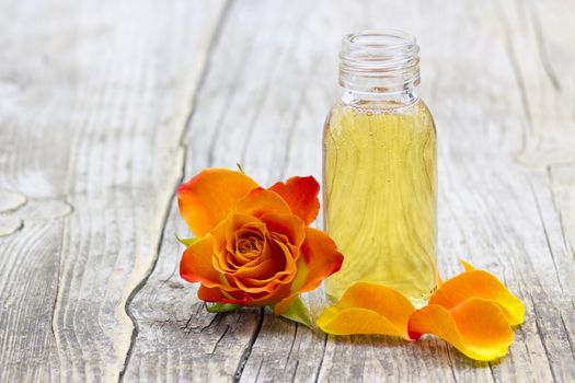 bath oil and orange rose on old wooden background