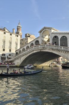 Gondola with tourists crossing the Rialto Bridge, one of the four bridges that spanning the Grand Canal in Venice, Italy. 