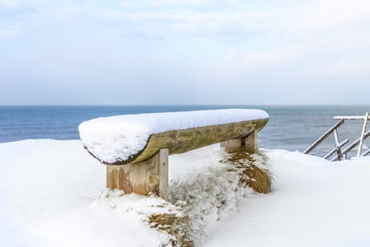 wooden bench covered with snow on the shore of the Baltic Sea, Ventspils, Latvia