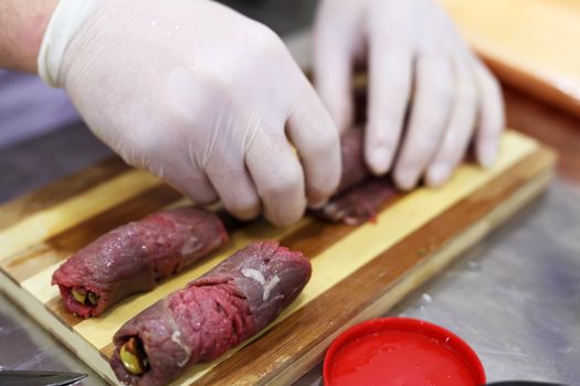 Chef hand preparing meat rolls on a wood cutter