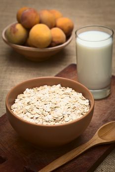 Bowl full of rolled oats with a glass of milk and peaches in the back photographed with natural light (Selective Focus, Focus one third into the oats)