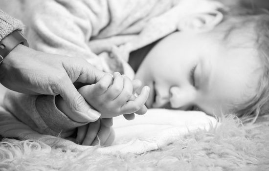 Closeup view of mother holding son's hand while he is sleeping