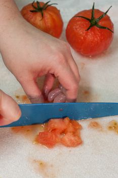 Fresh tomatoes being diced on a cutting board by a female chef with a ceramic knife.