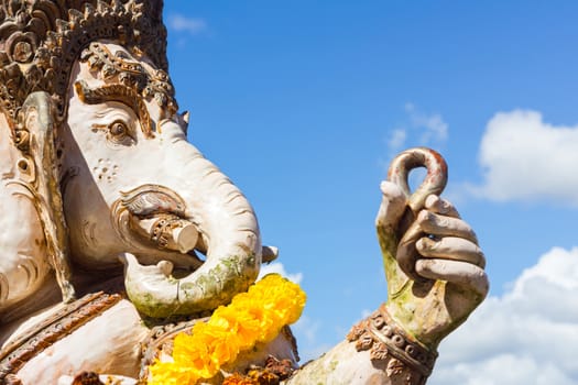 close-up statute of Ganesha outdoor against blue sky and white clouds.