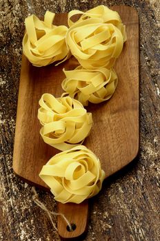 Nests of Raw Fettuccine In a Row on Cutting Board closeup on Rustic Wooden background