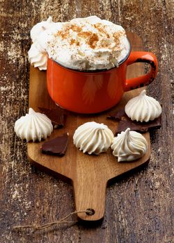 Meringues and Cup of Hot Chocolate with Whipped Cream and Cinnamon on Cutting Board on Rustic Wooden background