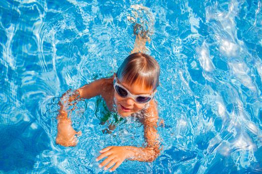 Cute happy little boy in goggles swimming and snorking in the swimming pool