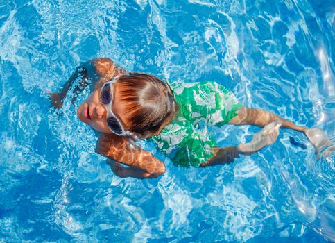 Cute happy little boy in goggles swimming and snorking in the swimming pool