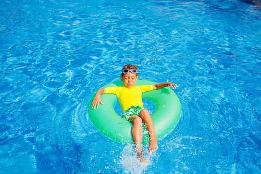 Cute little boy swims in a pool in an green life preserver