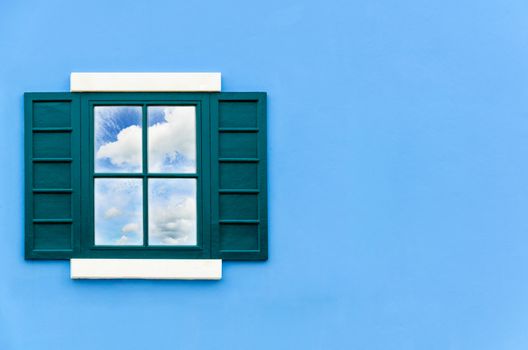 Sky and cloud reflection in green window glass on blue wall of house, Italy retro style