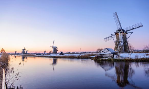 Sunrise over the windmills at the famous dutch UNESCO site Kinderdijk on a cold morning with some snow and reflection in the water of the canal in winter in the Netherlands.
