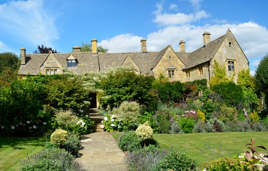 An English manor built out of Cotswold stone with stone tiles on the roof, called slates, with a garden full of flowers and a grass lawn in Chipping Campden, the Cotswolds, England, UK.