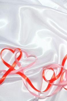 Red and pink satin glossy ribbon hearts over white silk background