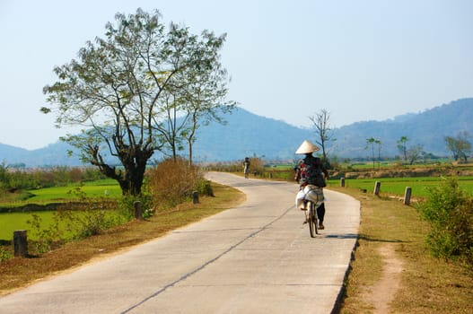 BUON ME THUOT, VIET NAM- FEB 7: Vietnamese woman riding bicycle on country road, beautiful of natural landscape at Daklak countryside, Vietnam, Feb 7, 2014