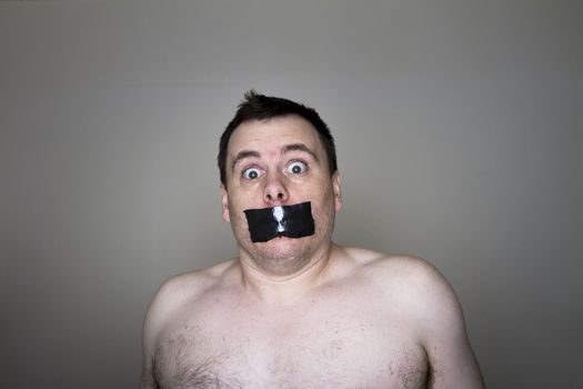 Man topless and having tape over his mouth being held against his will