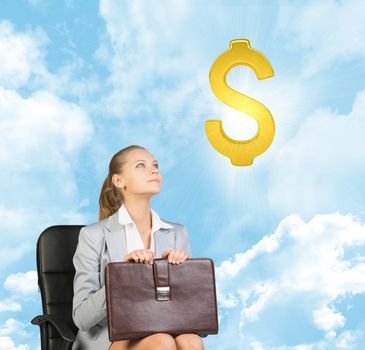 Businesswoman sitting on office chair, holding briefcase on her knees, looking up at golden dollar sign in the air, against blue sky with clouds