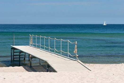 Wooden pier on the sandy beach over the green sea