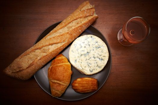 French blue cheese, baguette, croissant, madeleine and glass of wine on a table
