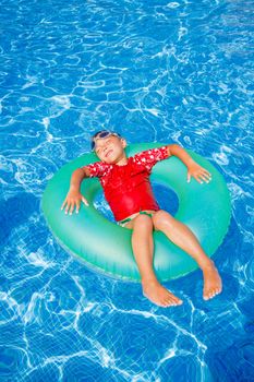 Cute little boy swims in a pool in an green life preserver