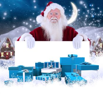 Santa looks over a sign against cute christmas village at night