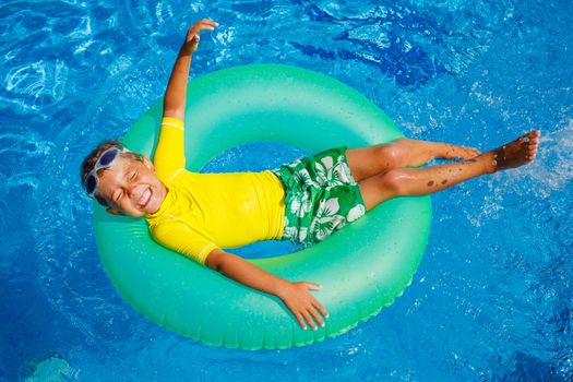 Cute little boy swims in a pool in an green life preserver