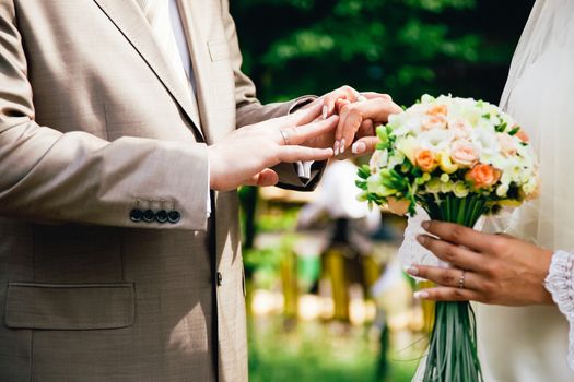 groom hand putting a wedding ring on the brides finger