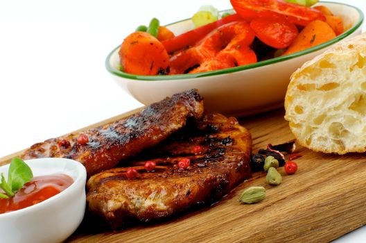 Arrangement of Roasted Pork Steaks with Grilled Vegetables, Tomato Sauce and Bread on Wooden Plate closeup on white background