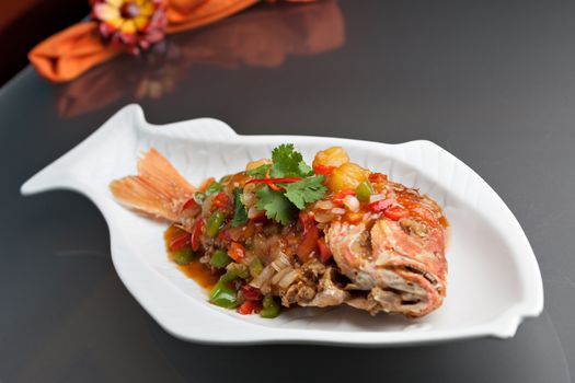 Freshly prepared Thai style whole fish red snapper dinner with tamarind sauce on a white fish shaped plate. Shallow depth of field.