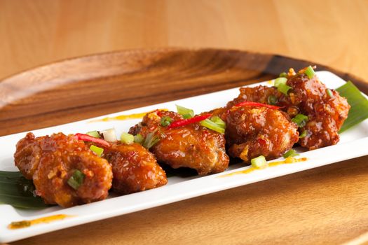 Thai style hot and spicy chicken wings appetizer on a contemporary white plate.