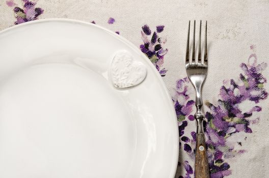 Detail of plate and fork laid on vintage wooden dining table with colorful tablecloth