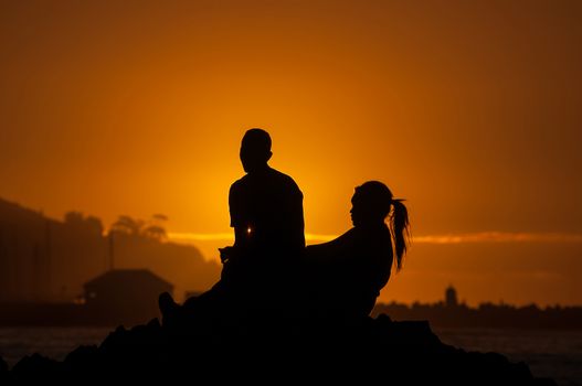 Silhouette of man and women against sunset over Gordons Bay in the Western Cape Province of South Africa
