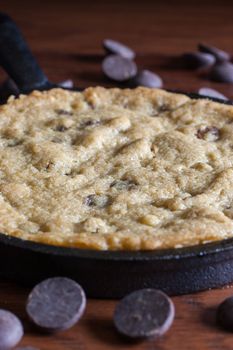 A personal-sized chocolate chip cookie in a cast iron pan with chocolate chips in the background.