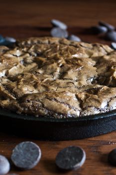 Fresh brownies in a cast iron pan with chocolate chips in the fore and background.