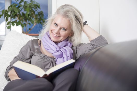 An image of a beautiful woman reading a book on her sofa