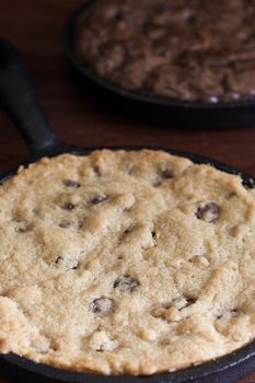 A personal-sized chocolate chip cookie in a cast iron pan with a brownie in the background.