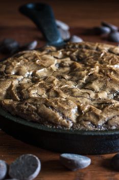 Fresh brownies in a cast iron pan with chocolate chips in the fore and background.