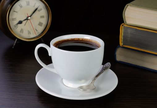 cup of coffee on the table with books and clock