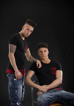 Two hip trendy male friends in studio shot, one is sitting on a chair