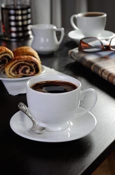 cup of coffee on the table with bread rolls and newspapers