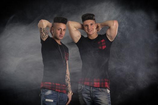 Two hip trendy male friends in studio shot smiling at camera, with smoke around them