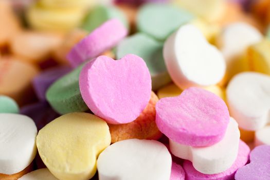 Pastel colored candy hearts in a pile on a white surface.