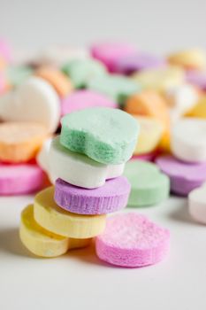 Pastel colored candy hearts in a pile on a white surface.