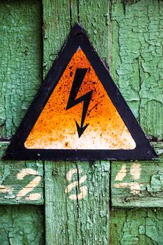 Old rusty warning high voltage sign on cracked green wooden surface