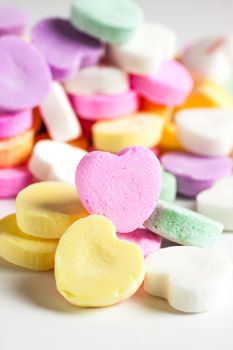 Pastel colored candy hearts in a pile on a white surface.