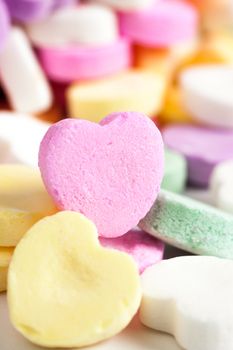 Pastel colored candy hearts in a pile on a white surface.