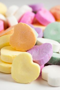 Pastel colored candy hearts in a pile on a white surface.